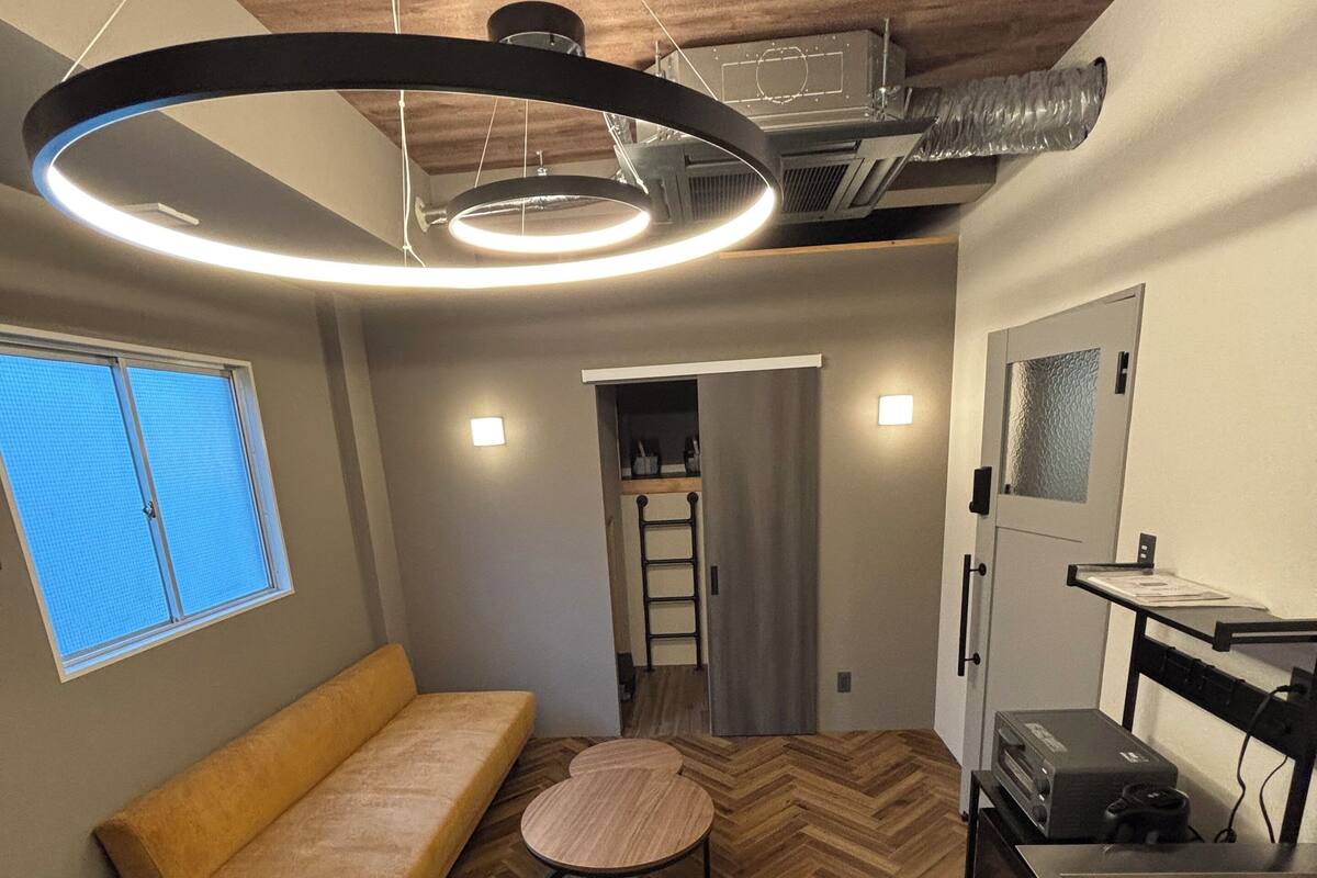 A modern interior with a sofa, a round table, a kitchenette, and a ceiling with exposed ductwork.