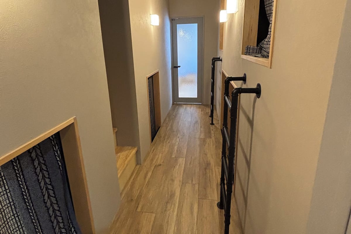 A narrow hallway with wooden flooring, a door at the end, and a wall-mounted radiator.