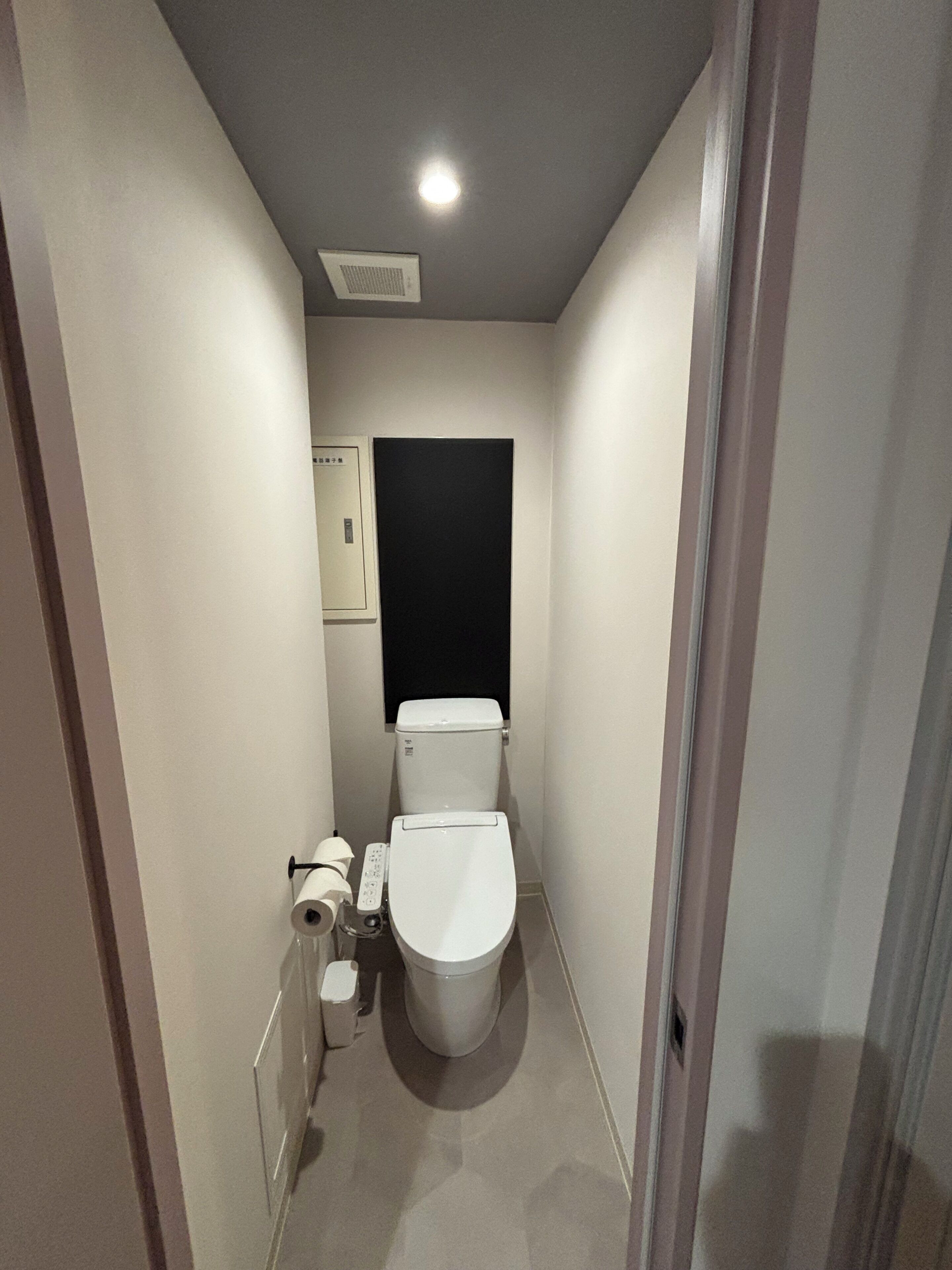 A narrow bathroom with a toilet, a bidet, and a toilet paper holder.
