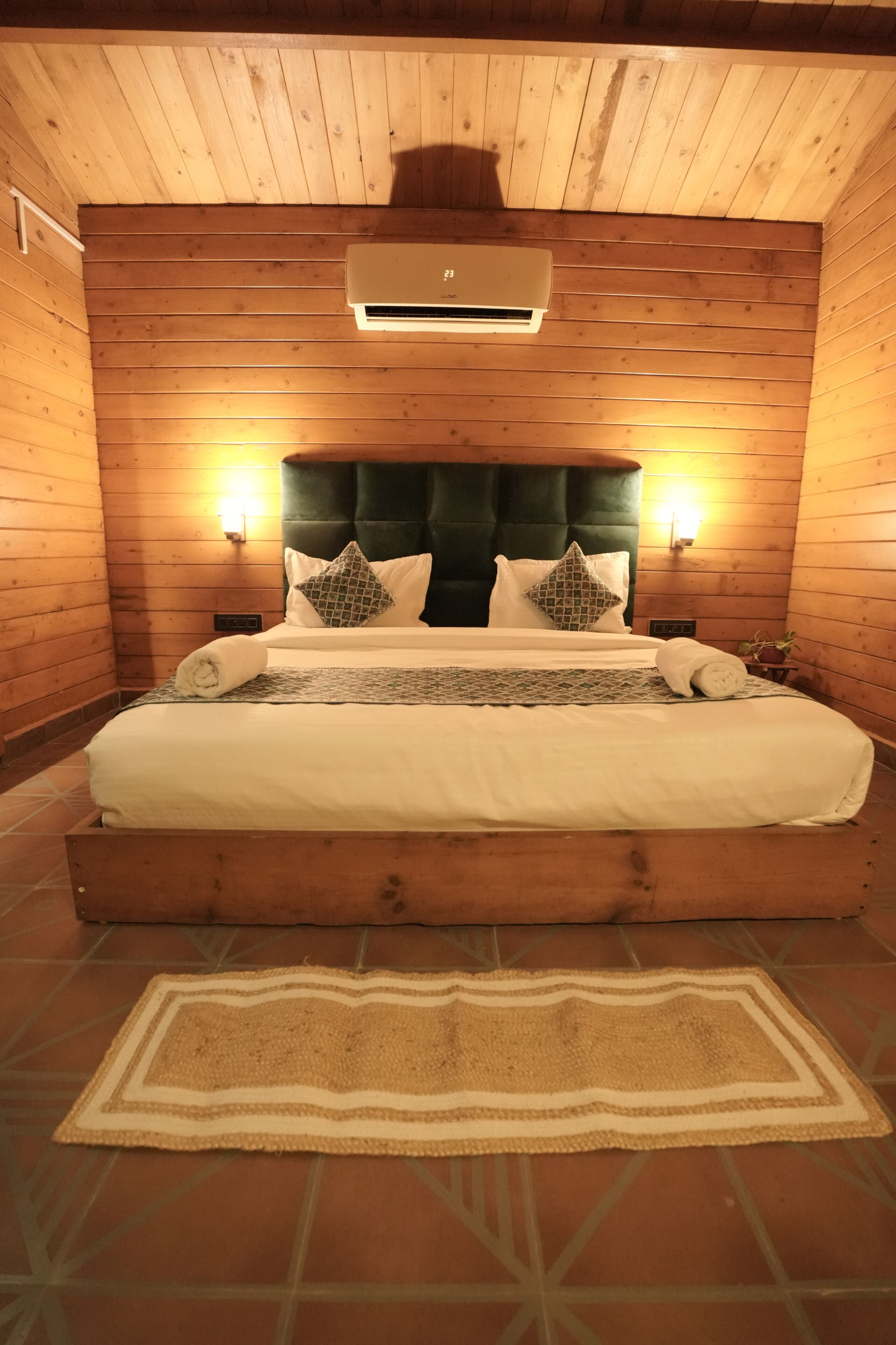 Una habitación con paneles de madera, una cama, dos lámparas de pared y un equipo de aire acondicionado.