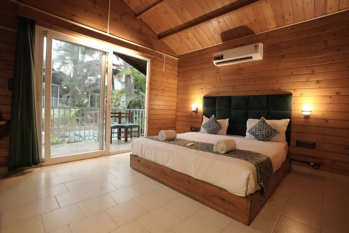 A wooden-paneled room with a bed, sliding glass doors to a balcony, and an air conditioning unit.