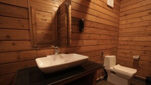 Un baño estilo cabaña de madera con lavamanos, espejo, inodoro y dispensador de toallas.