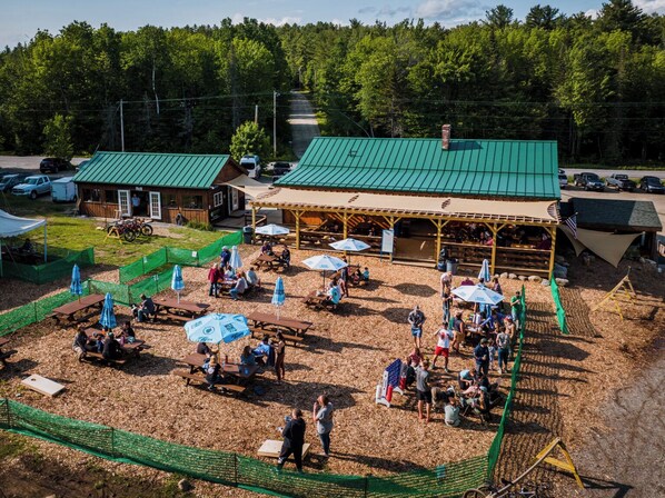 Un espace extérieur aménagé pour les repas, avec des tables de pique-nique et des parasols, le tout entouré d’une clôture en bois.