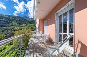 A balcony with a table and chairs, overlooking a mountainous landscape. - Hostdomus - Overseas Suite (Boissano)