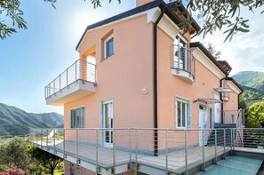 A two-story building with a balcony, a staircase, and a view of the mountains. - Hostdomus - Overseas Suite (Boissano)