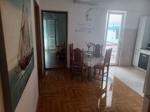 Ein Zimmer mit Holzboden, einem Esstisch mit Stühlen, einem Bild an der Wand und Blick durch eine Tür.