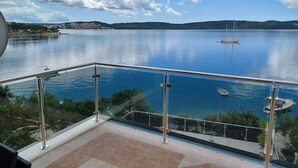 Ein Balkon mit Glasgeländer, der auf einen ruhigen See, eine entfernte Uferlinie und einen klaren Himmel blickt.