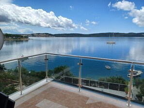 A balcony with a glass railing overlooking a calm lake, a distant shoreline, and a clear sky. - Apartments Marija (Trogir)