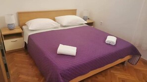 A neatly made bed with a purple bedspread and two white pillows, a wooden headboard, a nightstand with a lamp, and a folded towel on the bed. - Apartments Marija (Trogir)