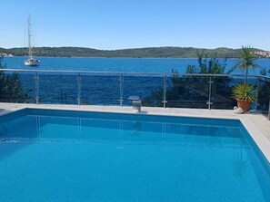 A swimming pool with a view of a sailboat on the water and a mountainous landscape in the background. - Apartments Marija (Trogir)