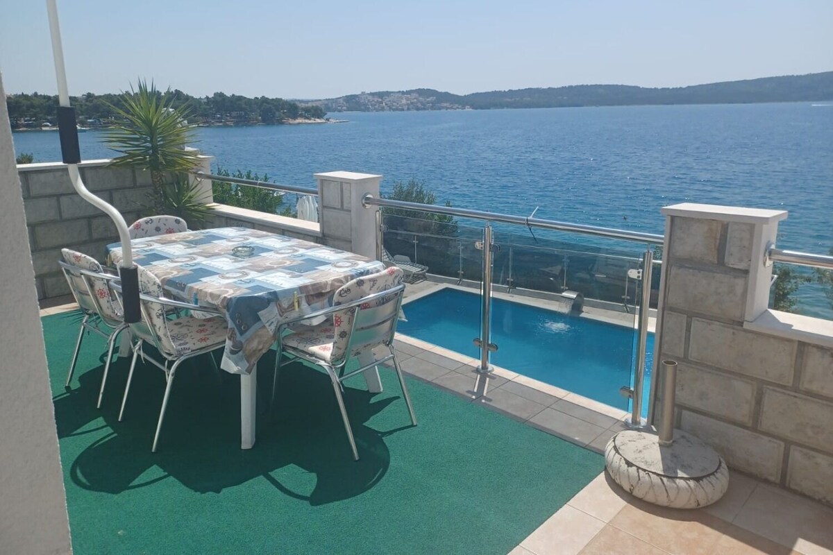 A balcony with a table and chairs, a swimming pool, and a view of the sea.