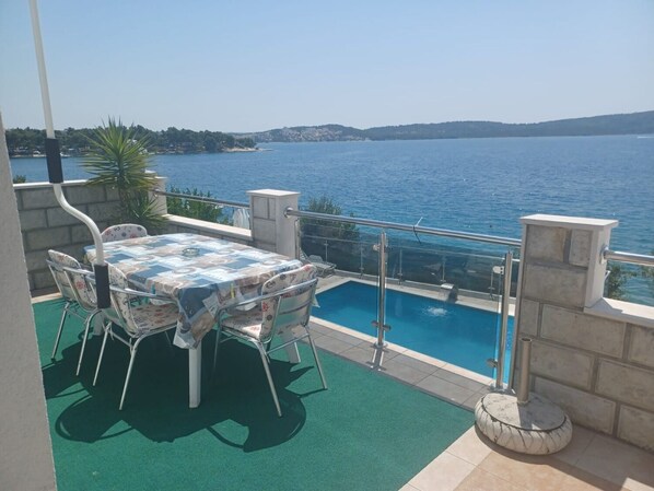 A balcony with a table and chairs, a swimming pool, and a view of the sea. - Apartments Marija (Trogir)