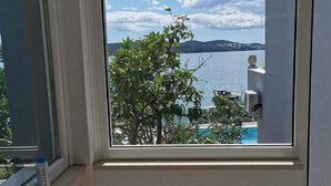 Ein Zimmer mit großem Fenster und Blick auf einen See, einen Baum und ferne Hügel.