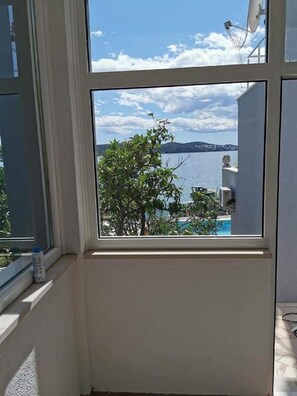 A room with a large window offering a view of a lake, a tree, and distant hills. - Apartments Marija (Trogir)