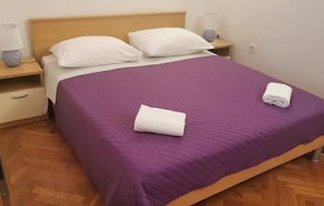 Ein Einzelbett mit lila Bettdecke, zwei weiße Kissen und zwei aufgerollte weiße Handtücher.