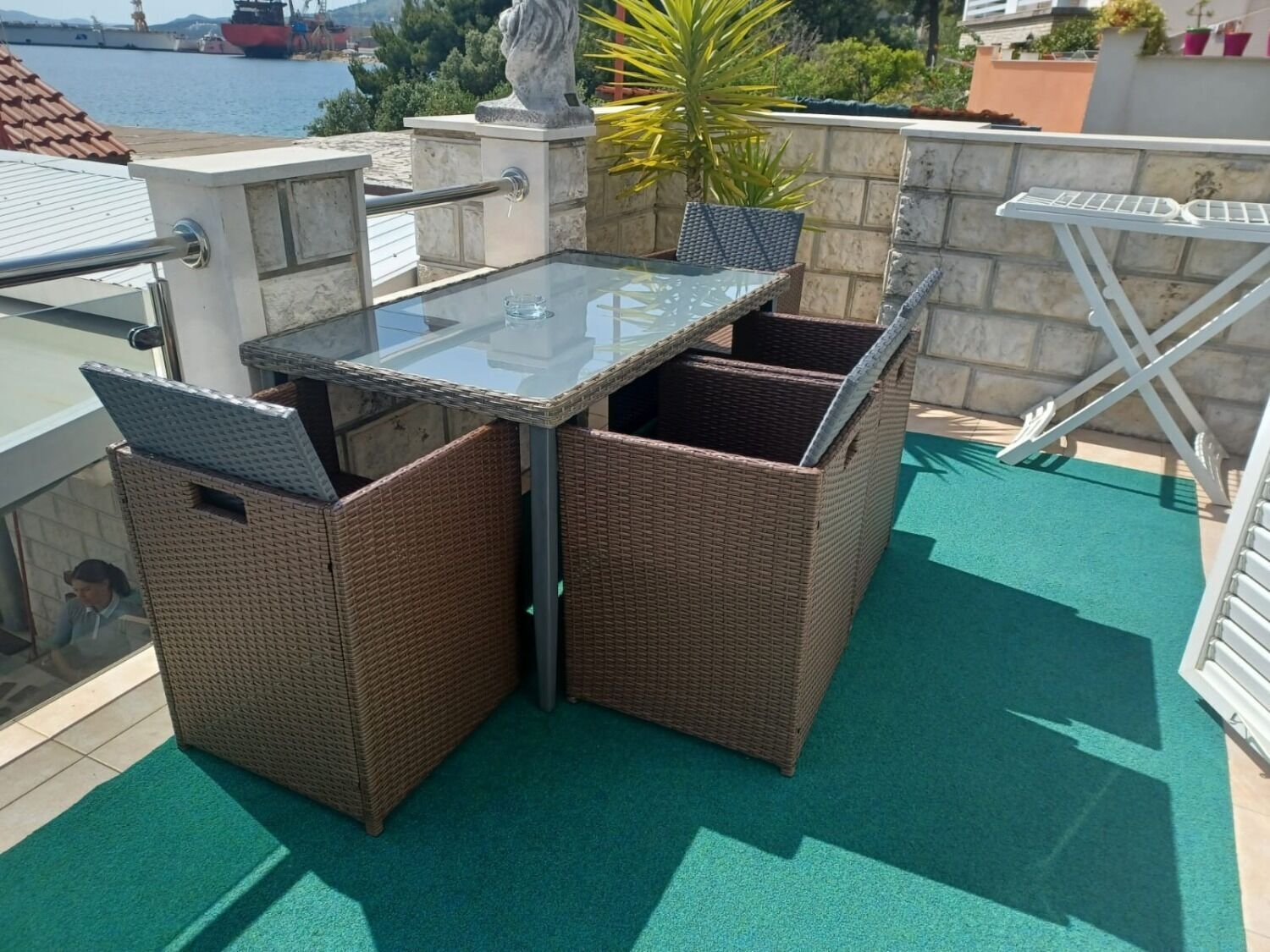 Ein Balkon mit Glastisch und Korbstühlen, mit Blick auf ein Gewässer und eine Skyline.