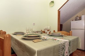 Ein Esstisch gedeckt mit Tellern, Gläsern und Besteck, ein Kühlschrank und eine Küchenzeile mit einer Mikrowelle.