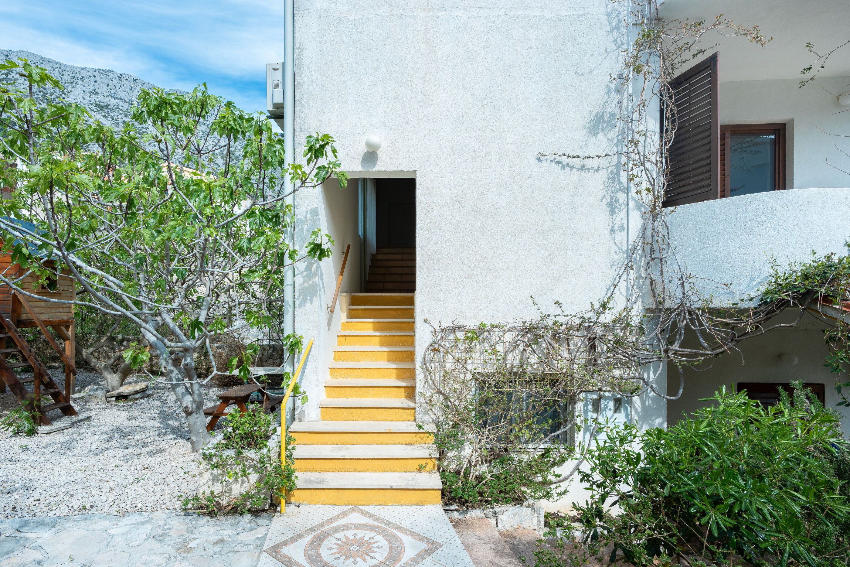 A building with a staircase leading to an entrance, surrounded by greenery and a clear sky.