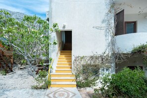 Ein Gebäude mit einer Treppe, die zu einem Eingang führt, umgeben von Grünpflanzen und blauem Himmel.