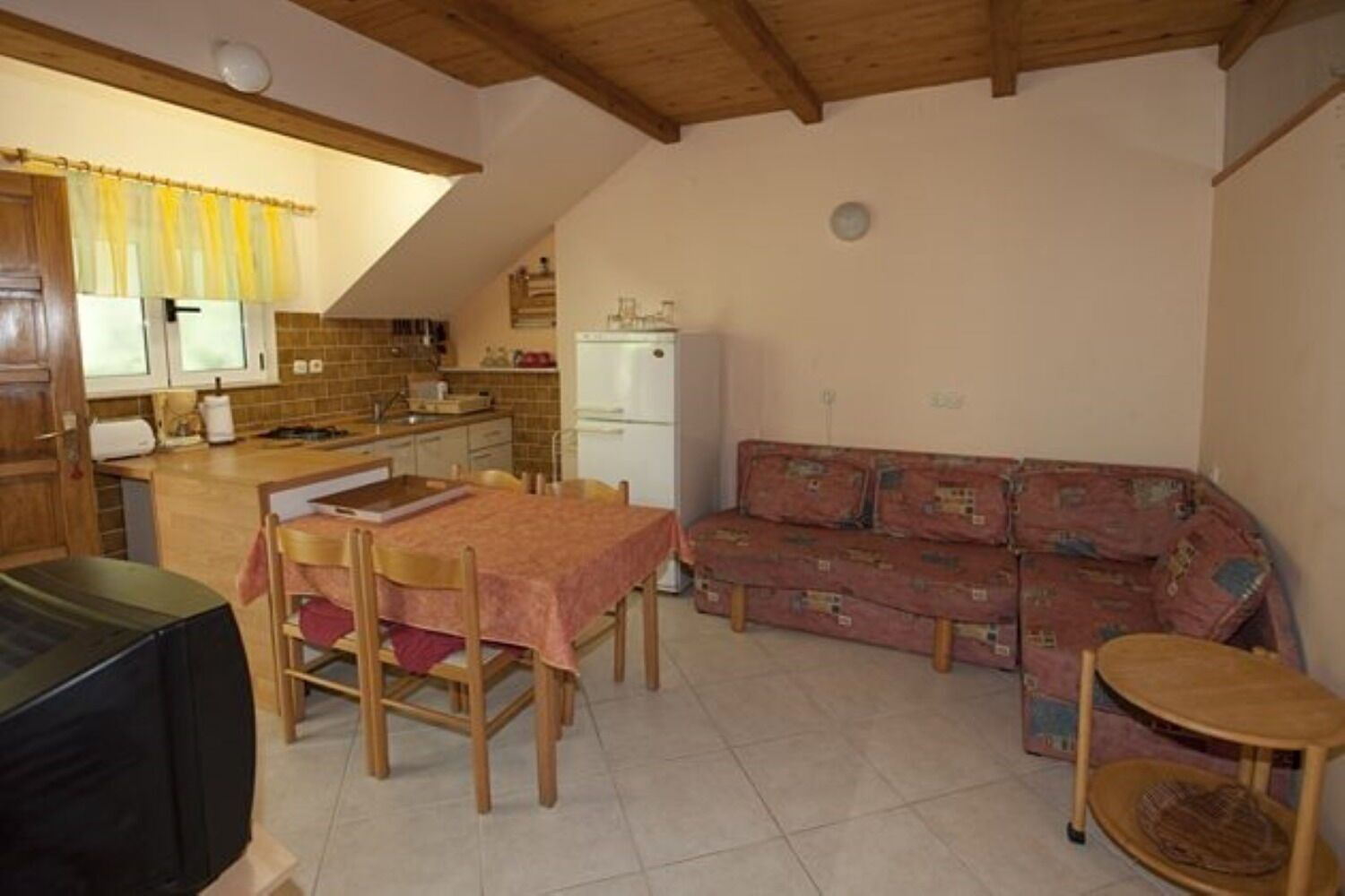 A cozy kitchen with a dining table, a sofa, and a TV.