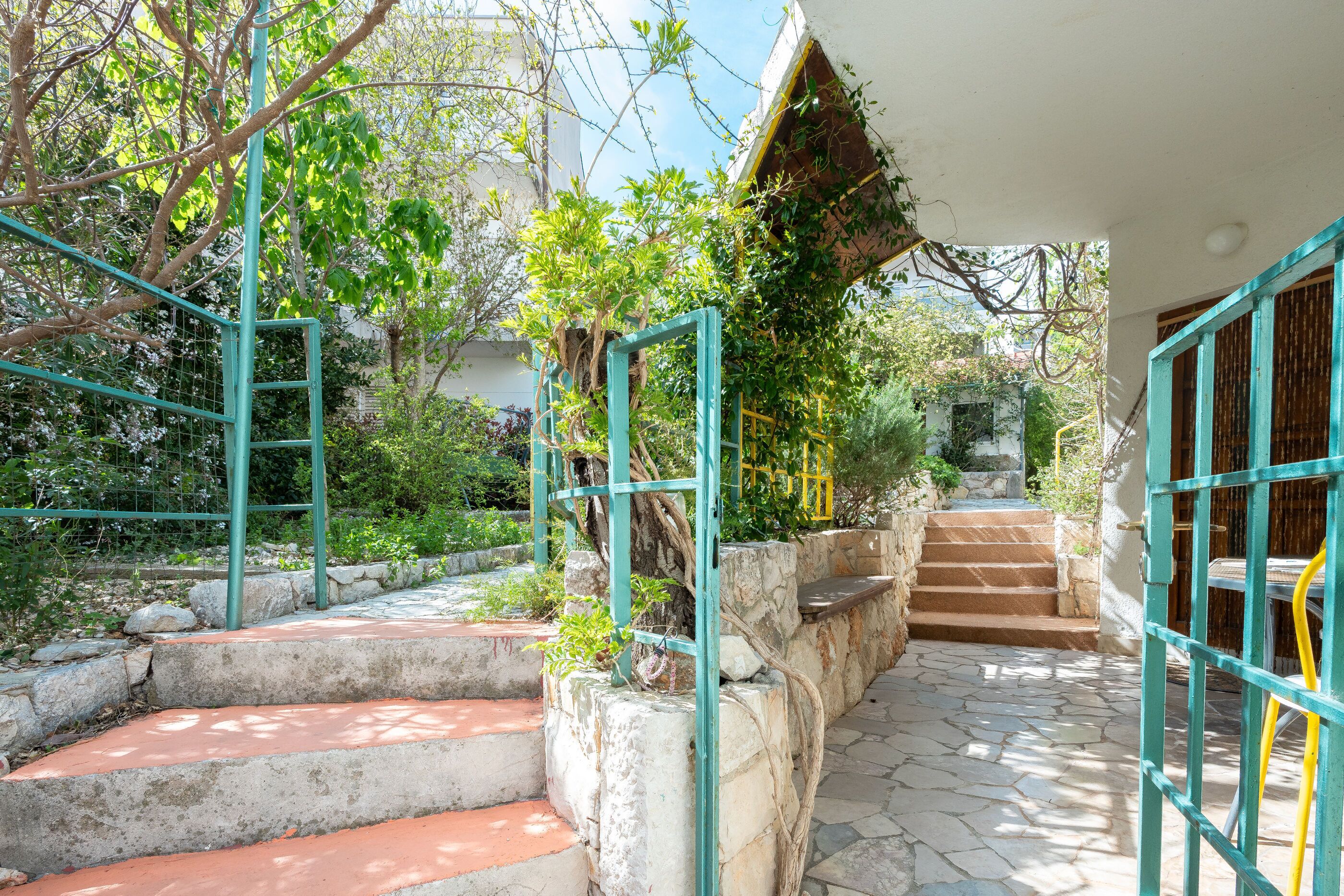A stone staircase leading to a building entrance, surrounded by greenery and a metal gate.