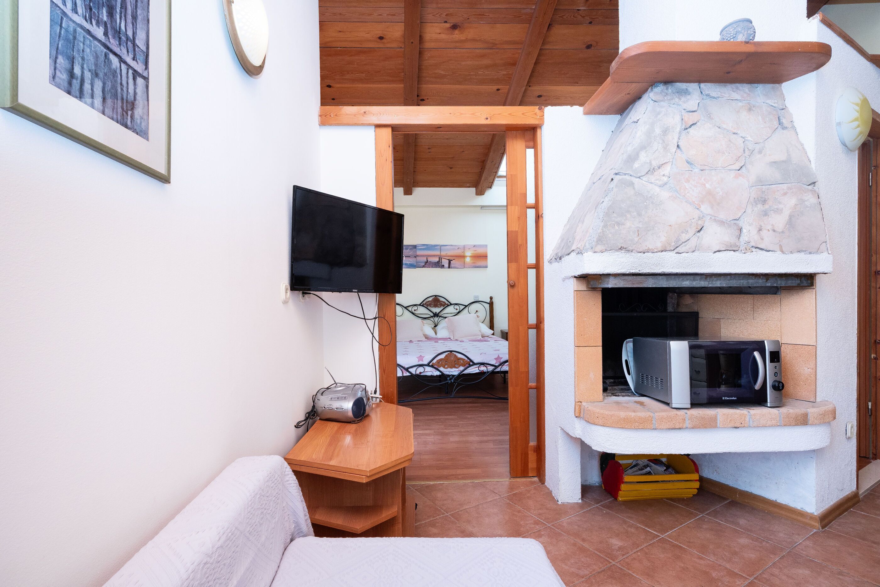A cozy room with a stone fireplace, a television, and a bed with a metal frame.