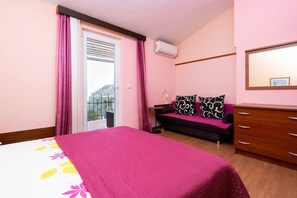A bedroom with a bed, a dresser, a bench, and a window with curtains. - Apartment Bezerusa (Podgora)