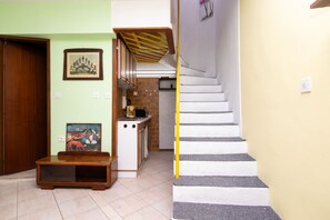 Eine Treppe mit weißen Stufen und einem gelben Geländer, die zu einem Küchenbereich mit einer gefliesten Spritzschutzwand und einem Holzkorpus führt.
