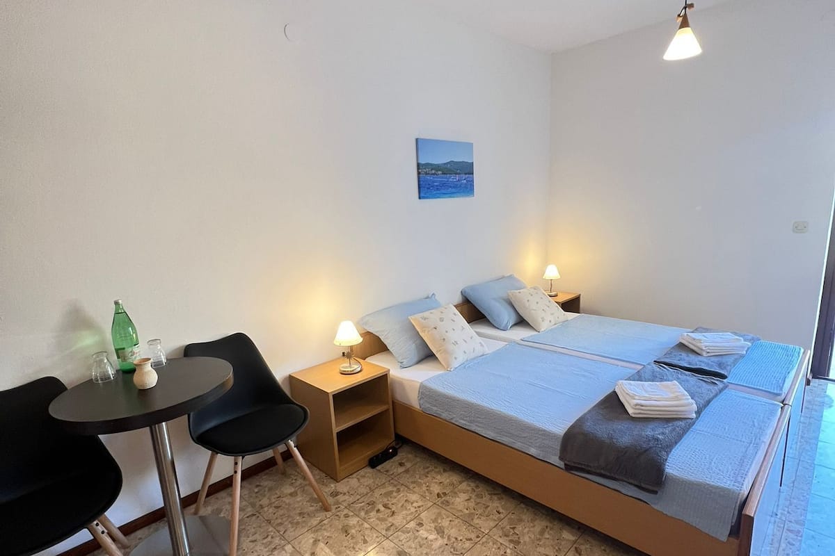 Une chambre à coucher comprenant un lit, des tables de chevet, une petite table avec des chaises, un tableau au mur et un sol carrelé.