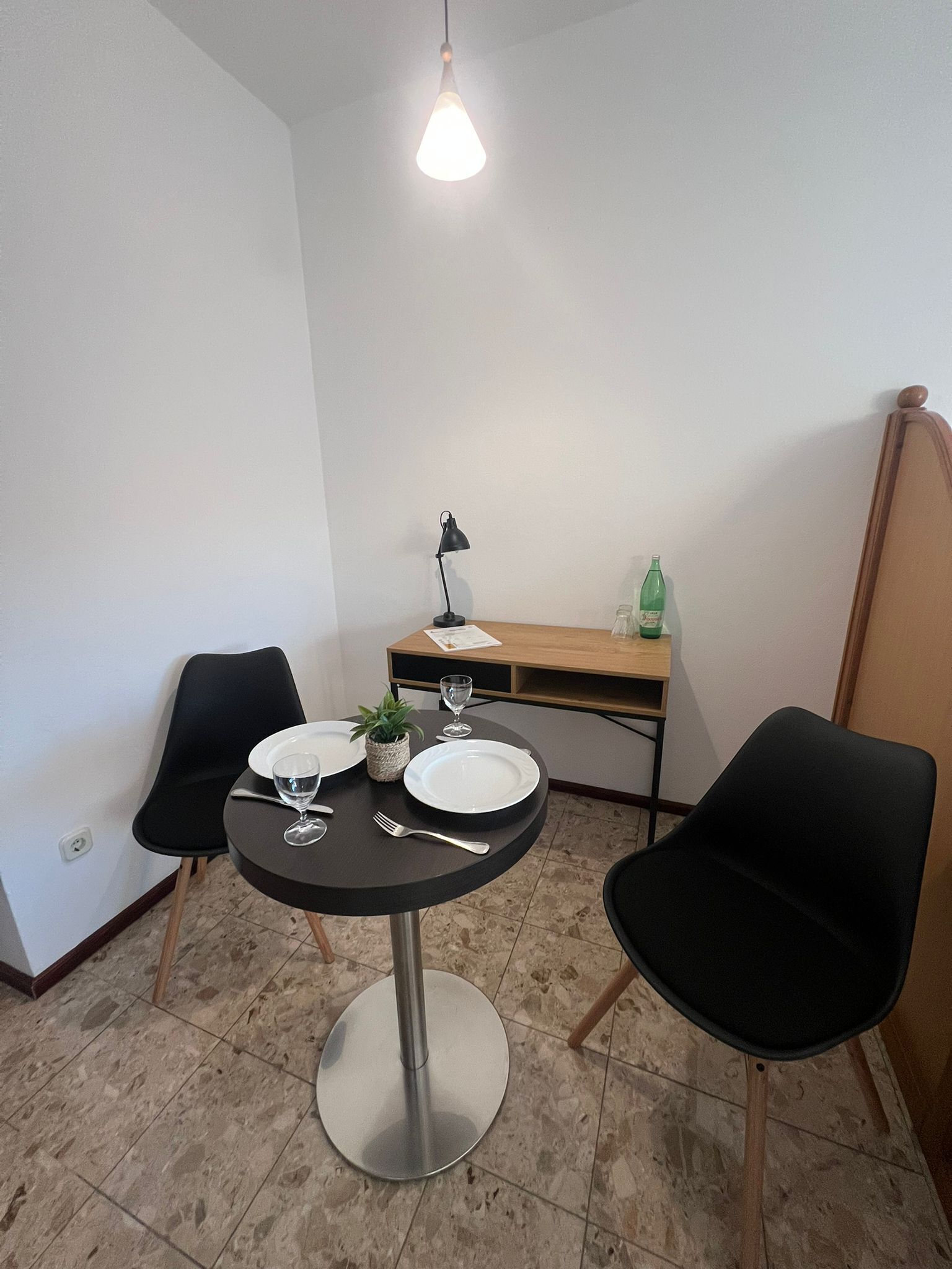 Ein kleiner Essbereich mit einem runden Tisch, zwei Stühlen, einer Lampe und einer Flasche auf einem Holztisch.