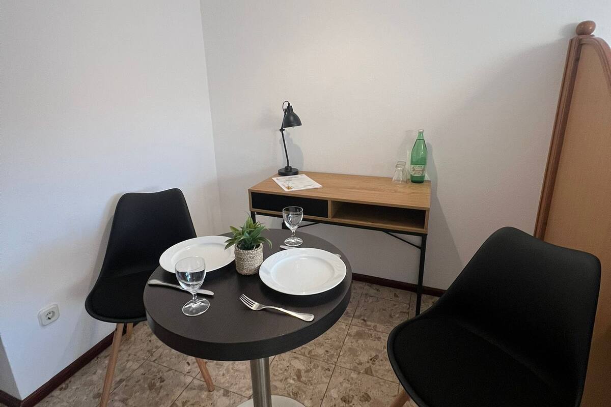 Un petit coin repas avec une table ronde, deux chaises, une lampe et une bouteille posée sur un bureau en bois.