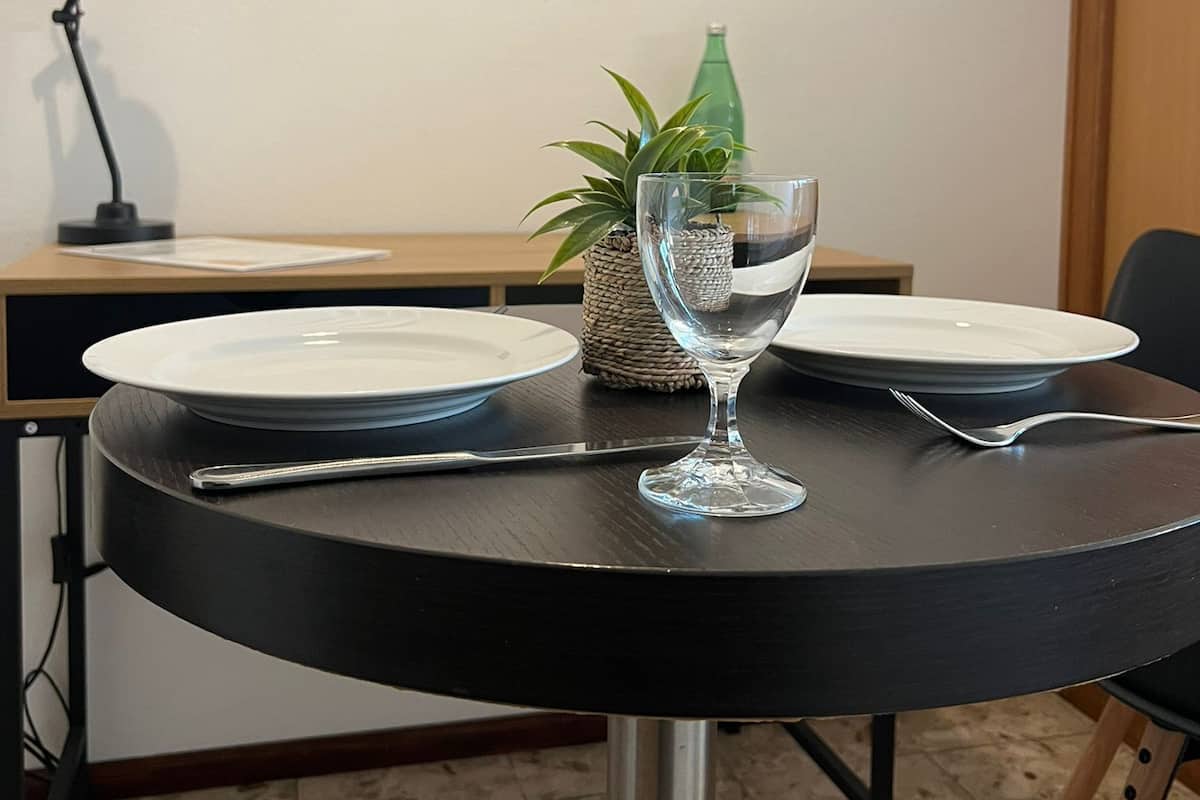 Une table à manger avec des assiettes, un verre et des couverts, une lampe et une petite plante.