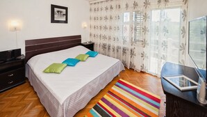 Ein Schlafzimmer mit Bett, Nachttisch, Fernseher und einem Fenster mit Vorhängen.