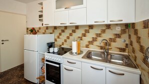 Eine kompakte Küche mit weißen Schränken, einem Kühlschrank von Bosch, einer Kaffeemaschine und einem Spülbecken.