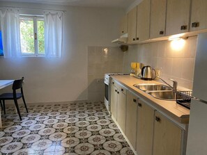 Eine kompakte Küche mit Essbereich, mit einem gemusterten Boden, einem Fenster mit Vorhängen und einfachen Küchenschränken.