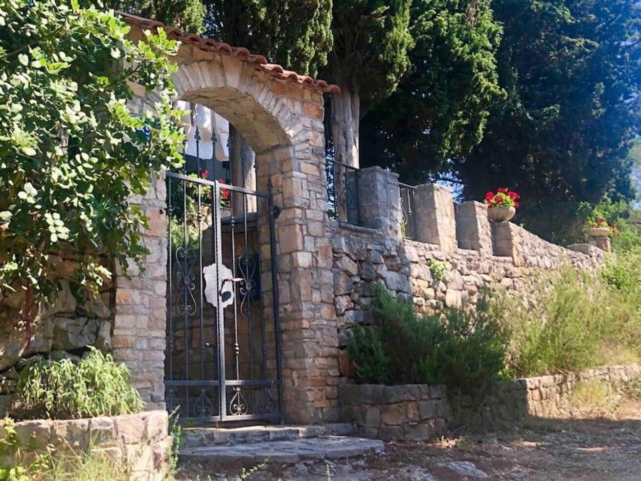 A stone archway leading to a gated entrance, surrounded by greenery and a stone wall.