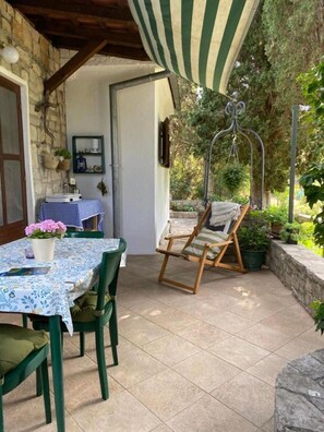 Eine Terrasse mit Tisch, Stühlen und einem Hängesessel, sowie eine Steinsäule.