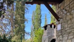 Ein Steinhaus mit Schornstein, einem Tisch mit Stühlen und einer Hängematte.