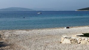 Ein Kiesstrand mit einer Steinmauer und einem Boot im Wasser.