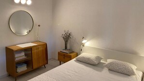 Ein Schlafzimmer mit einem Bett, Nachttischen, einer Kommode, einem Spiegel und Wandleuchten.