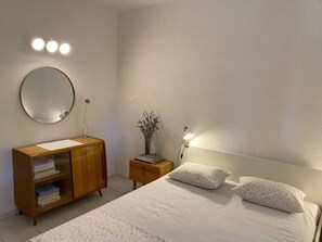 Ein Schlafzimmer mit einem Bett, Nachttischen, einer Kommode, einem Spiegel und Wandleuchten.