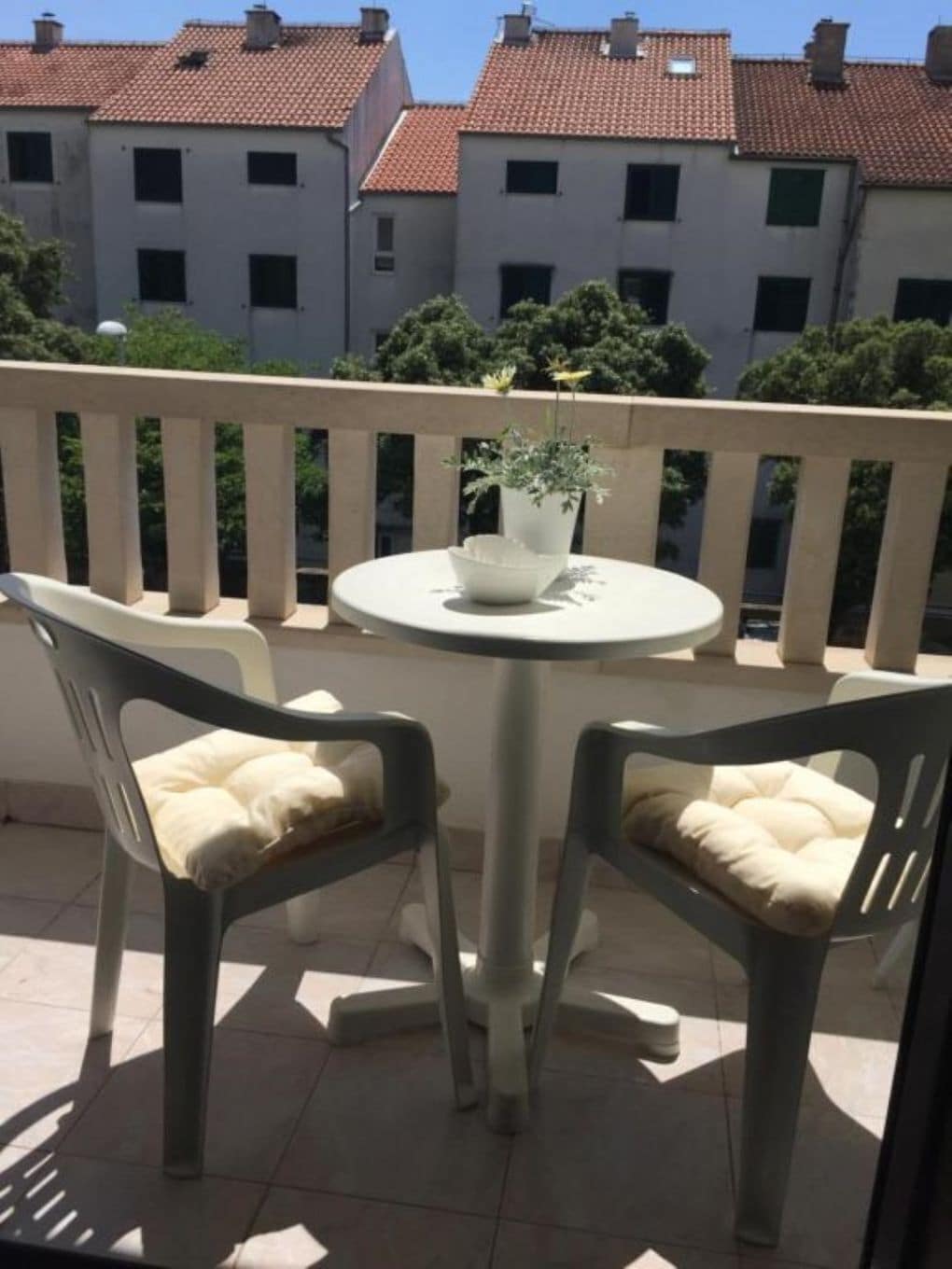 A balcony with two chairs and a table, a potted plant, and a railing.