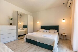 A hotel room with a bed, a dresser, a mirror, and a small table with a lamp. - Apartments and Room Tattoo (Makarska)