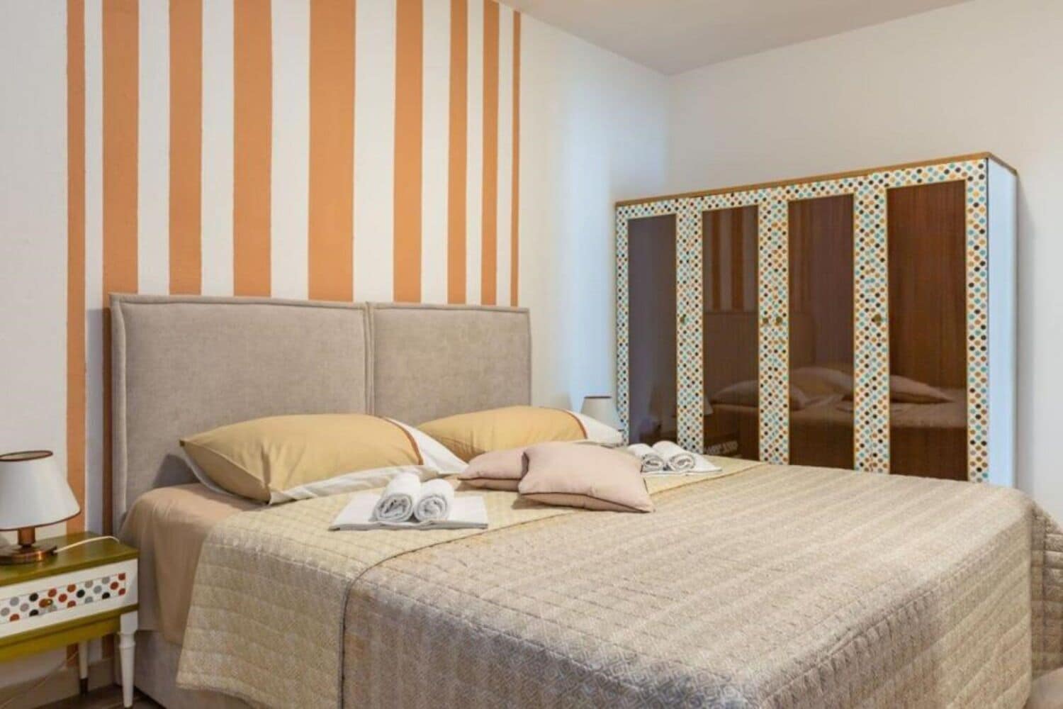 Ein Hotelzimmer mit Bett, Kissen, einem Nachttisch mit Lampe und einem Schrank mit Muster.