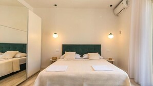 Un lit double bien fait, avec une tête de lit verte, deux tables de chevet avec des lampes et un grand miroir sur un des murs.