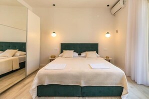 A neatly made double bed with a green headboard, two bedside tables with lamps, and a large mirror on one wall.