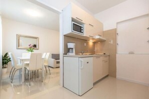 A compact kitchen with a microwave, coffee maker, and a small sink. There is a dining area with chairs and a table. - Apartments and Room Tattoo (Makarska)