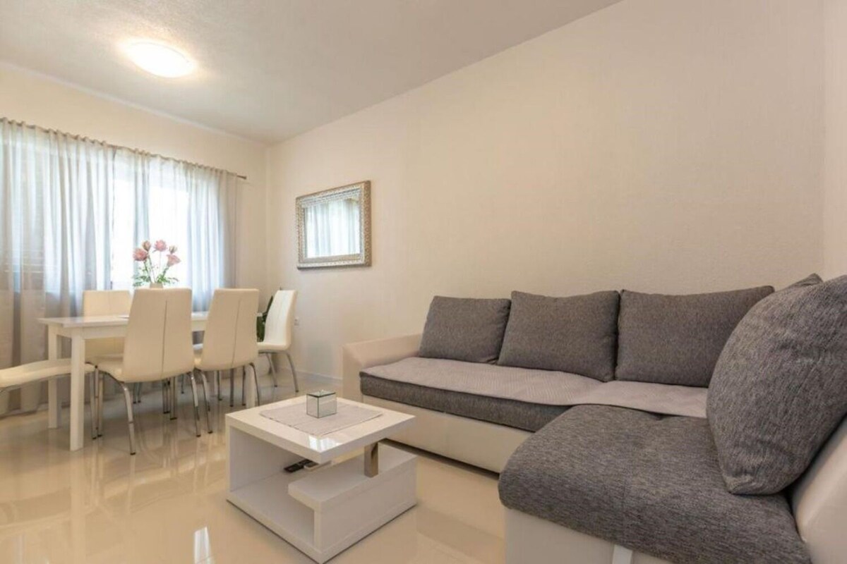 A modern living room with a grey sofa, a dining table with chairs, and a small white side table.
