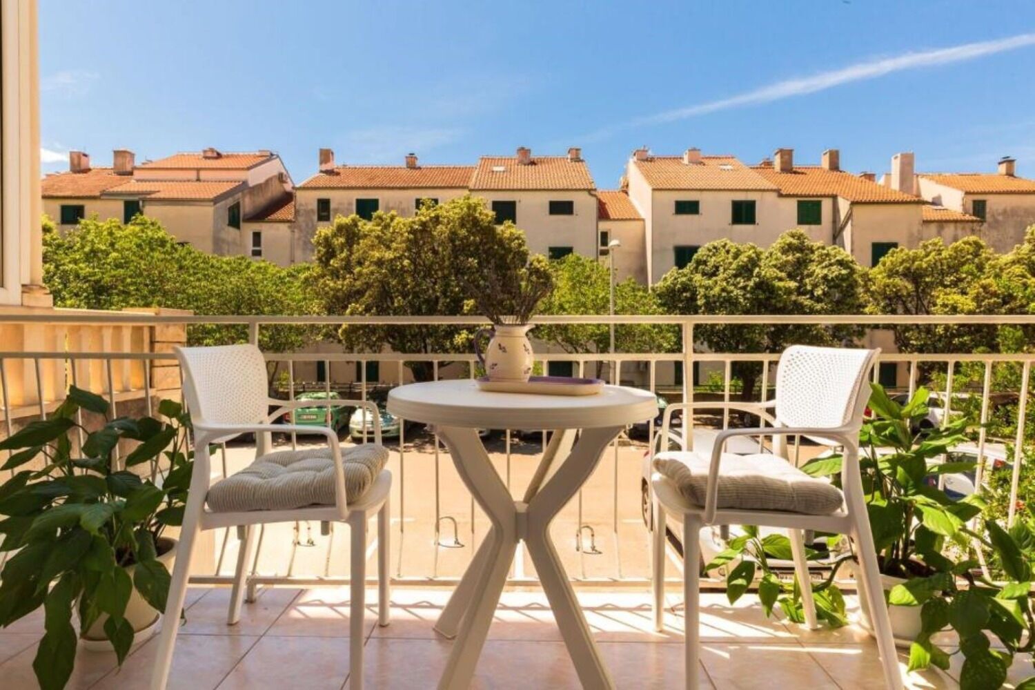A balcony with two white wicker chairs, a small round table, and a potted plant.