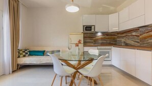 Une cuisine moderne avec des meubles blancs, une table à manger en verre et un luminaire suspendu.